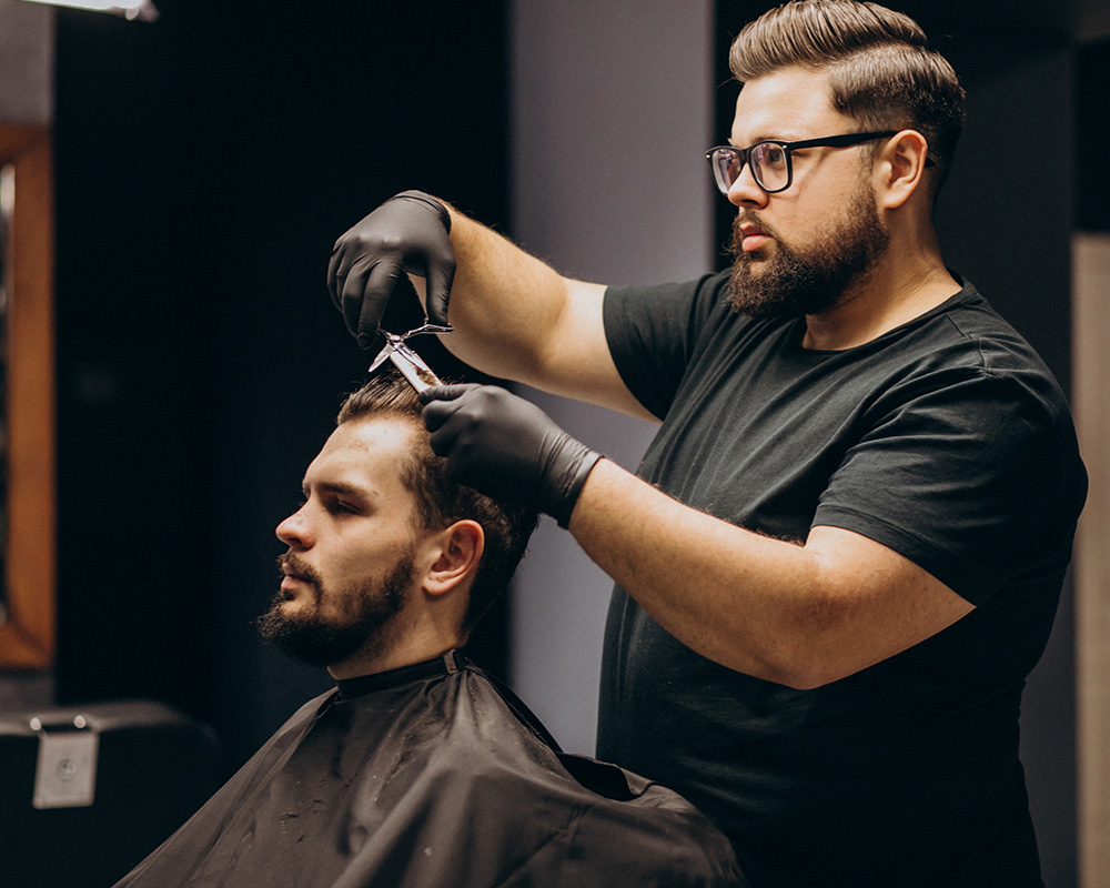 Pote de pasta modeladora Barba Macho sobre bancada de barbearia, ao lado de navalha e tesoura